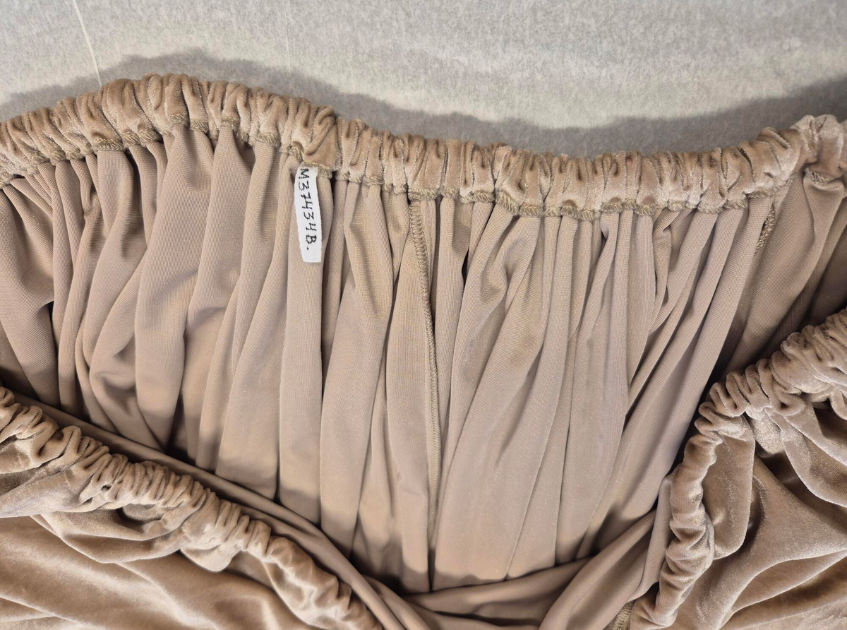 Byxor i harem-modell uppsydda i rosa-beige sammetstyg och champangefärgade applikationer samt stenar. Applikationerna är i form av blommor och löv. Fastklistrade på tyget i en större vertikal form i mitten av byxorna. Ihopsydd med 4 tygpaneler, ej fodrad. Samansatt med raksöm och vid vissa delar overlocksöm. Byxbenen avslutas med muddar som stängs med 2 hakar och hyskor på vardera ben. Muddarna har ett mellanlägg för att ge struktur. Midjan har en kanal för ett vitt snöre som knyts för att dra åt midjan och stänga byxorna. 

