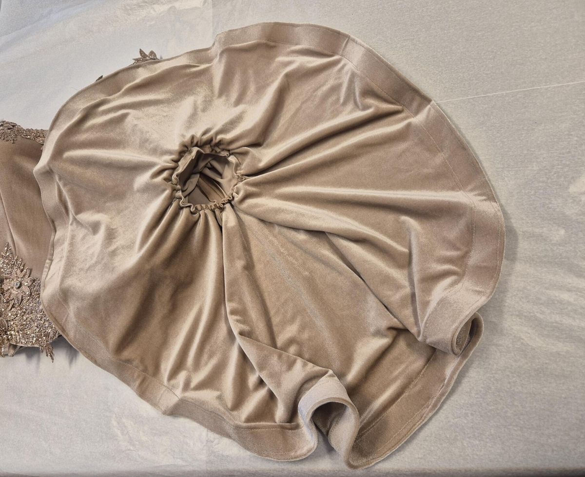 Strukturerad överdel uppsydd i rosa-beige sammetstyg och champangefärgade applikationer samt stenar.  Applikationerna är i form av blommor och löv. Fastklistrade på tyget. De är placerade runt den runda ringningen, lätt nedåt vid axeln samt nedre delen av plagget. Torson är uppdelad i 10 tygpaneler ihopsydda med raksöm, fodrad med ett beige tyg (möjligen baksidan av sammetstyget). Stängda kanaler på insidan för korsettbening.16 stycken totalt.  Nedre kanten av överdelen är benad. Inbyggda kupor. Korsettstängning på baksidan med extra tygstycke för att dölja huden under. Stängningen består av 10 stycken tyg öglor på vardera sidan av överdelen och ett tillhörande band.  

Ärmarna är fästa till överdelen med zick-zack söm. Raka, smala ärmar till armbågen, därefter öppnas de upp till en vid fallande form. Ofodrade vid den smala delen. Den vida delen är fodrad med samma sammetstyg som yttertyget. 
Dom smala delarna är ett tygstycke vardera. De vida delarna är ett separat tygstycke vardera och fästa till resterande ärm med raksöm, lätt veckade. 
Ärmarna avslutas med en fållad kant som innehåller ett stabiliserande mellanlägg. Applikationerna samma som ovan men placerade kring armbågen - där den smala delen av ärmen möter den vida delen. 




