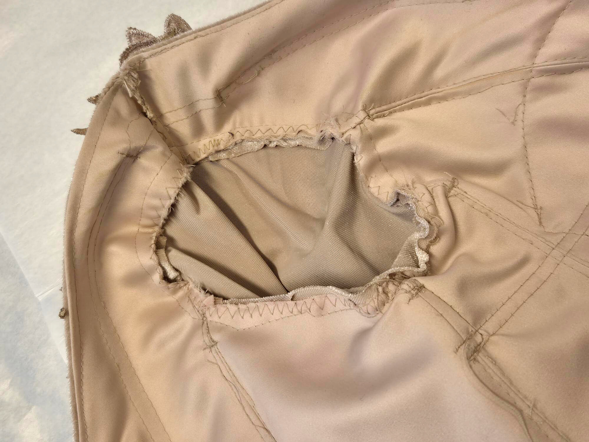 Strukturerad överdel uppsydd i rosa-beige sammetstyg och champangefärgade applikationer samt stenar.  Applikationerna är i form av blommor och löv. Fastklistrade på tyget. De är placerade runt den runda ringningen, lätt nedåt vid axeln samt nedre delen av plagget. Torson är uppdelad i 10 tygpaneler ihopsydda med raksöm, fodrad med ett beige tyg (möjligen baksidan av sammetstyget). Stängda kanaler på insidan för korsettbening.16 stycken totalt.  Nedre kanten av överdelen är benad. Inbyggda kupor. Korsettstängning på baksidan med extra tygstycke för att dölja huden under. Stängningen består av 10 stycken tyg öglor på vardera sidan av överdelen och ett tillhörande band.  

Ärmarna är fästa till överdelen med zick-zack söm. Raka, smala ärmar till armbågen, därefter öppnas de upp till en vid fallande form. Ofodrade vid den smala delen. Den vida delen är fodrad med samma sammetstyg som yttertyget. 
Dom smala delarna är ett tygstycke vardera. De vida delarna är ett separat tygstycke vardera och fästa till resterande ärm med raksöm, lätt veckade. 
Ärmarna avslutas med en fållad kant som innehåller ett stabiliserande mellanlägg. Applikationerna samma som ovan men placerade kring armbågen - där den smala delen av ärmen möter den vida delen. 



