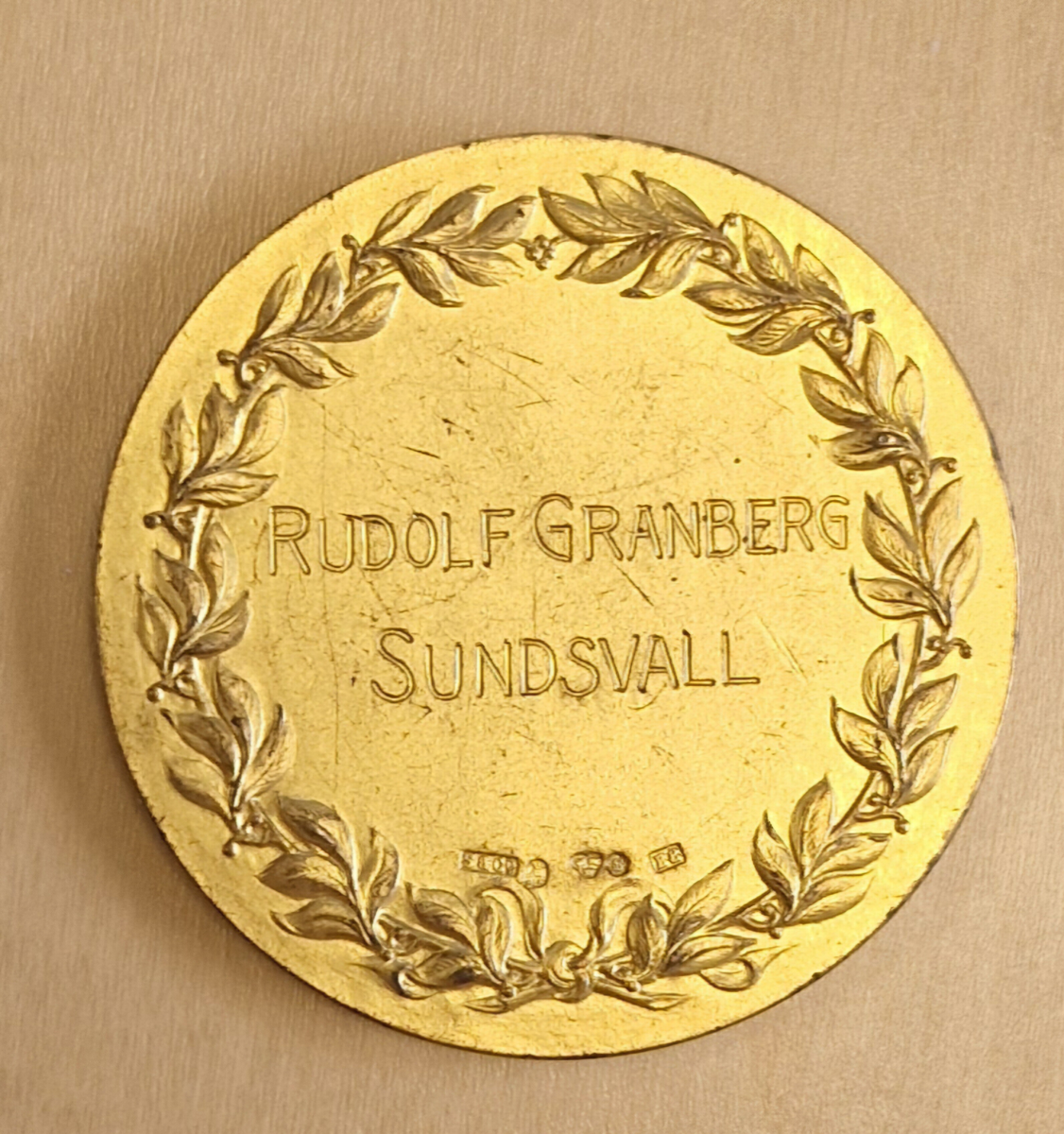 Medalj av metall. Framsidan: ett krönt stadsvapen, Sundsvallsutställningen 1928. Baksidan: Inom en krans: Rudolf Granberg Sundsvall och svårlästa stämplar: ?, 5809, kattfot, 33 eller BB. Gåva av Owe Walter.

Anm: Under högsommaren 1928, den 21 juni till den 29 juli anordnades en sommarutställning i Sundsvall. Ungefär 850 utställare från de mest varierade verksamheter lockade till sig mängder med besökare.

Året innan, 1927, hade Ostkustbanans räls anlagts och tågen till Sundsvall hade börjat gå längs kusten. Det underlättade kommunikationerna betänkligt, och var en orsak till att utställningen förlades hit. Olof Ahlström, Sundsvalls Tidnings fd chefredaktör var initiativtagare och generalsekreterare för mässan.

Alltihop invigdes den 21 juni av kronprinsen Gustaf Adolf och hans hustru Louise Mountbatten. Redan den första dagen löste 8000 personer in sig på området och det var festyra i staden.

Utställningen låg inne på de olika skolgårdarna längs Skolhusallén och fortsatte en bit upp mot Södermalm där ett nöjesfält slagit upp sina karuseller.

En hel del nya byggnader fick uppföras, bland annat en stor maskinhall och en 112 meter lång automobilhall på läroverksplan. En viadukt över järnvägen och en restaurant på folkskoleplanen samt en byggnad för hästutställningen byggdes också upp enbart för utställningen. Att det fanns stora hallar både för bilar och hästar visar på den brytningstid som tjugotalet innebar när det gäller den allt mer utbredda motoriseringen.

På nöjesfältet fanns attraktioner som en dansbana och ett dåtidens lustiga hus med rörliga golv, rullande trottoarer och skrattspeglar. Ett spektakulärt högt torn i sex våningar med rutschkanor i spiral reste sig också högt över åskådarna på marken.

Utställningen som pågick i en månad var den största i sitt slag som då hållits i Norrland och lockade utställare inom näringar som exempelvis industri, hantverk, livsmedel, jordbruk, konst och turism. Föreningar som Skidfrämjandet var också på plats, mitt i sommarvärmen, för att marknadsföra Storlien som skidort.

I samband med utställningen anordnades även två motortävlingar, en mer professionell tävling mellan Stockholm och Sundsvall och en "turisttävling" mellan Falun och Sundsvall. Fler tävlingar, i form av spinntävlingar och annat hantverk var också populärt och utställningar av både frön och konst var viktiga delar.
Källa: Sundsvalls Tidning 8 september 2013 