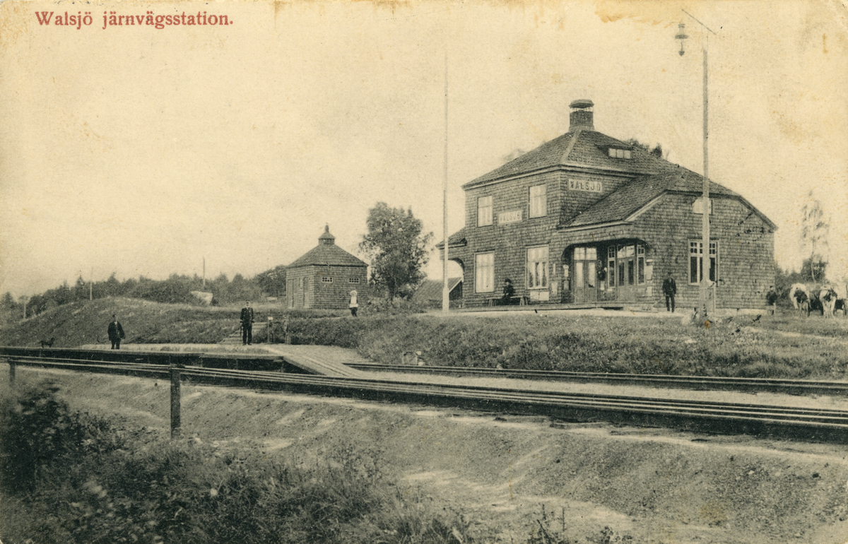 "Walsjö järnvägsstation". Valsjö, stationshuset med järnvägsrälsen i förgrunden. Människor står på perrongen och vid huset.

Transport, kommunikation, SNJ, Stockholm-Nynäs järnväg, Nynäsbanan.
