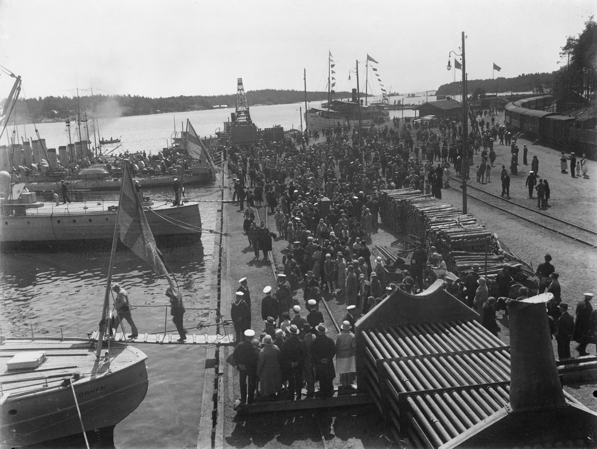 Gotlandskajen vid avfärd till invigningen av Älvsnabbsmonumentet. Hamnen är full av människor och på de militära båtarna, bland annat pansarskeppet Gustav V. 

Sjöfart, försvar, militär, flottan, historiska händelser.