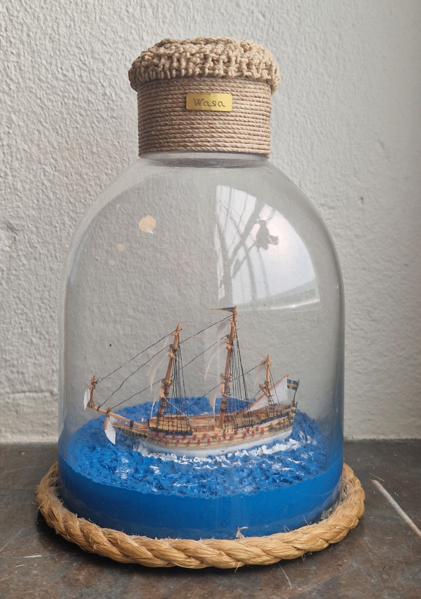 Stående flaskskepp, kantat med rep nedtill. En liten metallskylt på båda sidor "Wasa". Tillverkare Per Hugo Hedebrand. Flaskan är förseglad med mässingsplakett och makramé, plakett med inristad monogramsignering, A P H + ett ankare. Gåva av Ing Marie Hedebrand, Sundsvall. 