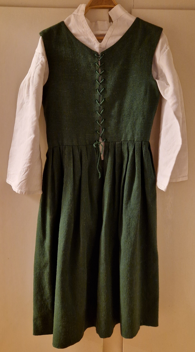 Folkdräkt från Ådals-Liden. Livkjol, överdel, förkläde, halskläde, kjolsäck, mössa, strumpbyxor och skor. Halsklädet, metallspännet på kjolsäcken, strumpbyxorna och skorna är inköpta. Skorna med etikett inuti: "Britta från Wiskania". Svensk kvalitet. Storlek 4½. Kjolsäcken är märkt med initialerna I F, (Ing-Marie Frisendal) och 1954. Gåva av Ing-Marie Hedebrand, Sundsvall. Tillverkad av Ing-Maries syster, Margareta Frisendal.
Anm: Folkdräkten från Ådals-Liden, en del av Ångermanland, har livkjol av helylle med empireskärning, ett vitt linneförkläde (modell södra dräkten) och en bindmössa i rött eller grönt, inspirerad av södra dräkten. Överdelen är en linnesärk med hålsöm vid ärmsluten och en utåtvikt fåll vid halsringningen. 
En kjolsäck, som tillhör dräkten, är gjord av blått ylletyg med applikationer i rött och gult, med ett centralt placerat hjärta och andra dekorativa former. 
Ådals-Lidens folkdräkt är en del av de två typerna av ångermanländska folkdräkter, den södra och den norra, som presenterades av Ångermanlands hemslöjdsförening år 1922. 
Källa: https://www.draktnyckel.se/adalsliden/