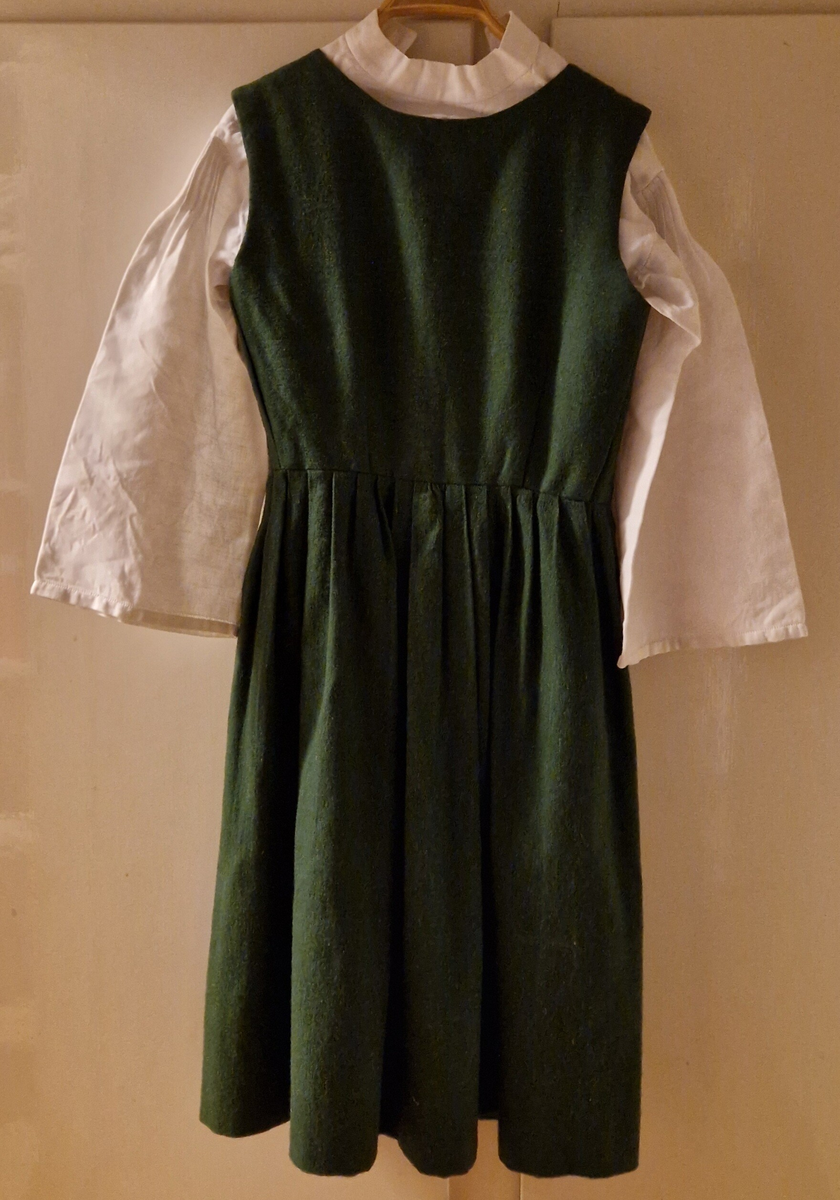 Folkdräkt från Ådals-Liden. Livkjol, överdel, förkläde, halskläde, kjolsäck, mössa, strumpbyxor och skor. Halsklädet, metallspännet på kjolsäcken, strumpbyxorna och skorna är inköpta. Skorna med etikett inuti: "Britta från Wiskania". Svensk kvalitet. Storlek 4½. Kjolsäcken är märkt med initialerna I F, (Ing-Marie Frisendal) och 1954. Gåva av Ing-Marie Hedebrand, Sundsvall. Tillverkad av Ing-Maries syster, Margareta Frisendal.
Anm: Folkdräkten från Ådals-Liden, en del av Ångermanland, har livkjol av helylle med empireskärning, ett vitt linneförkläde (modell södra dräkten) och en bindmössa i rött eller grönt, inspirerad av södra dräkten. Överdelen är en linnesärk med hålsöm vid ärmsluten och en utåtvikt fåll vid halsringningen. 
En kjolsäck, som tillhör dräkten, är gjord av blått ylletyg med applikationer i rött och gult, med ett centralt placerat hjärta och andra dekorativa former. 
Ådals-Lidens folkdräkt är en del av de två typerna av ångermanländska folkdräkter, den södra och den norra, som presenterades av Ångermanlands hemslöjdsförening år 1922. 
Källa: https://www.draktnyckel.se/adalsliden/