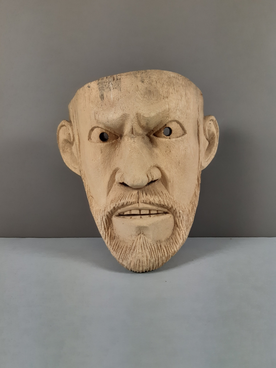 Snidad mask av ljust trä föreställande en arg man med skägg och mustasch by Okänd konsntär