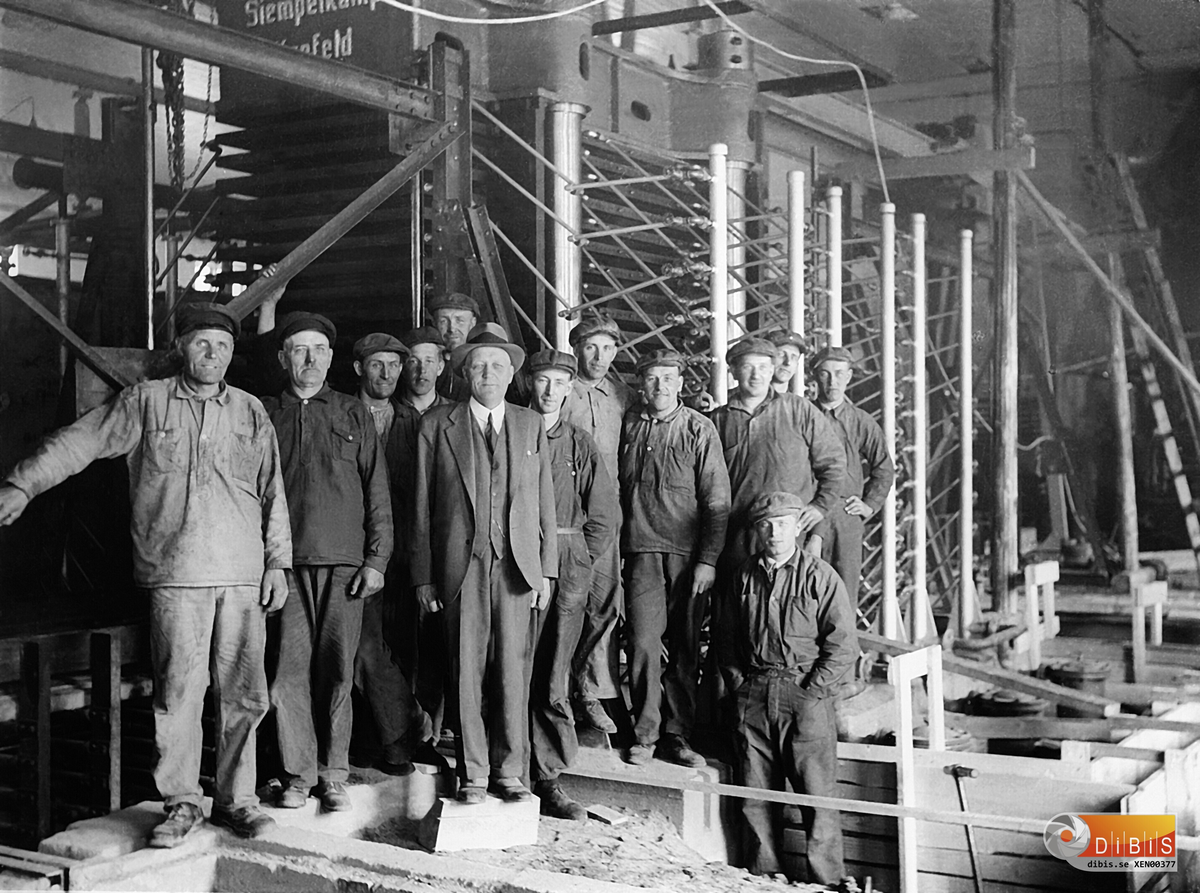 MIDNÄSFABRIKEN
1936 inköptes en ny press för tillverkning av träfiberplattor. Pressen hette Siempelkampf och var tillverkad i Krefeld, Tyskland. Det tog i en pressening 20 st. 12 fotspannor. Bilden är tagen vid monteringen av pressen. Fr.v Per Persson Lust Per i Berga, arbetare från Arbrå, Per-Olov Nordfeldt, Sievert Engström, Valfrid Persson Österböle, Disponent Anders Jonsson Höjen, ErikJonsson Jonpers i byn Fotografen, Olov Redåker V. Höle, Olle Sjöberg Polberg, en Arbråbo, Erik Eriksson Hedbacka, Edvard Wallin Svedja och framför de andra en tysk montör. Foto Erik Jonsson.