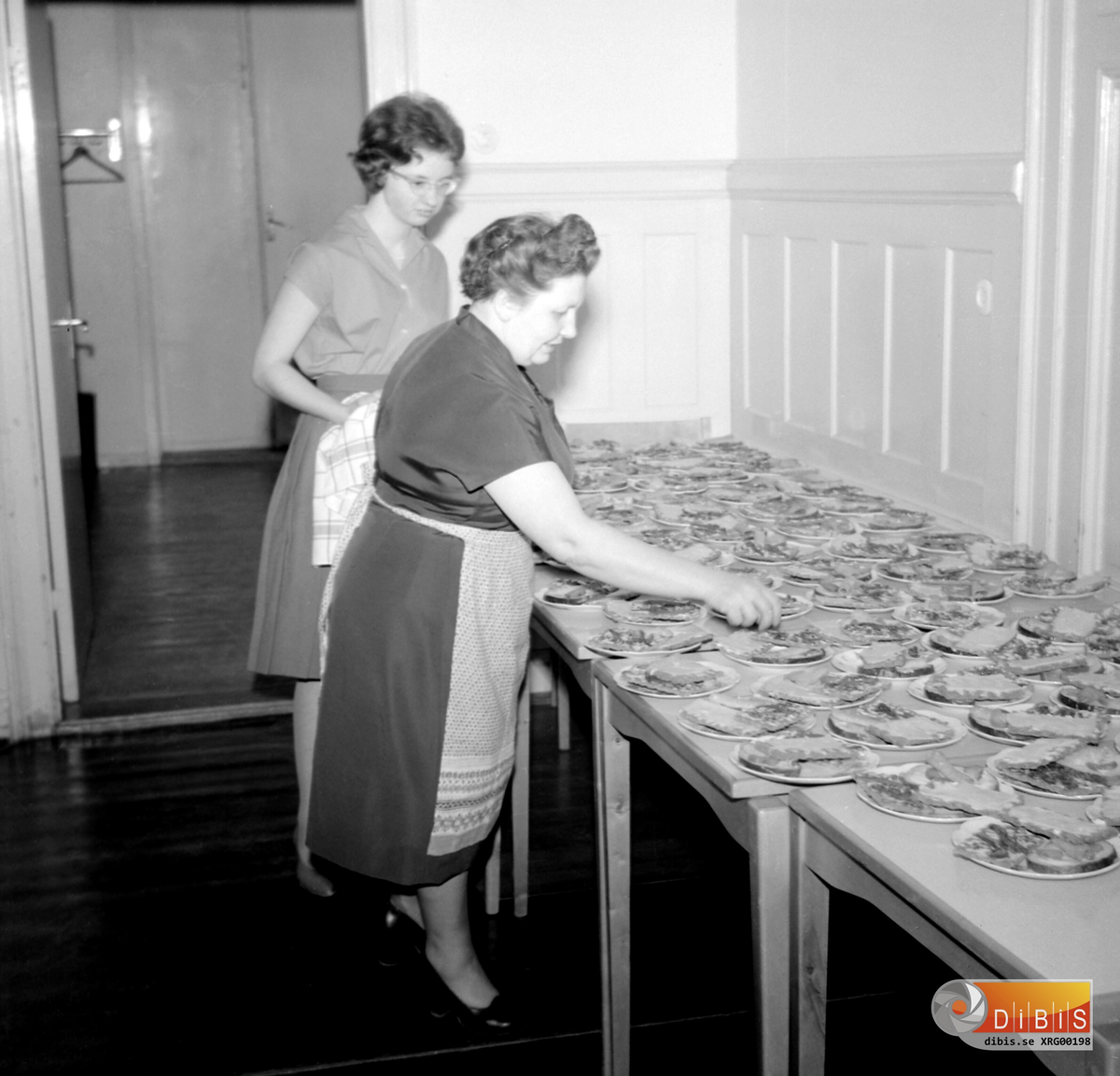 Kerstin Persson och Maj Nordlund (1912-2005) förbereder inför servering vid ett samkväm på den gamla IOGT-lokalen på Köpmangatan 9 i Söderhamn. Året är 1961