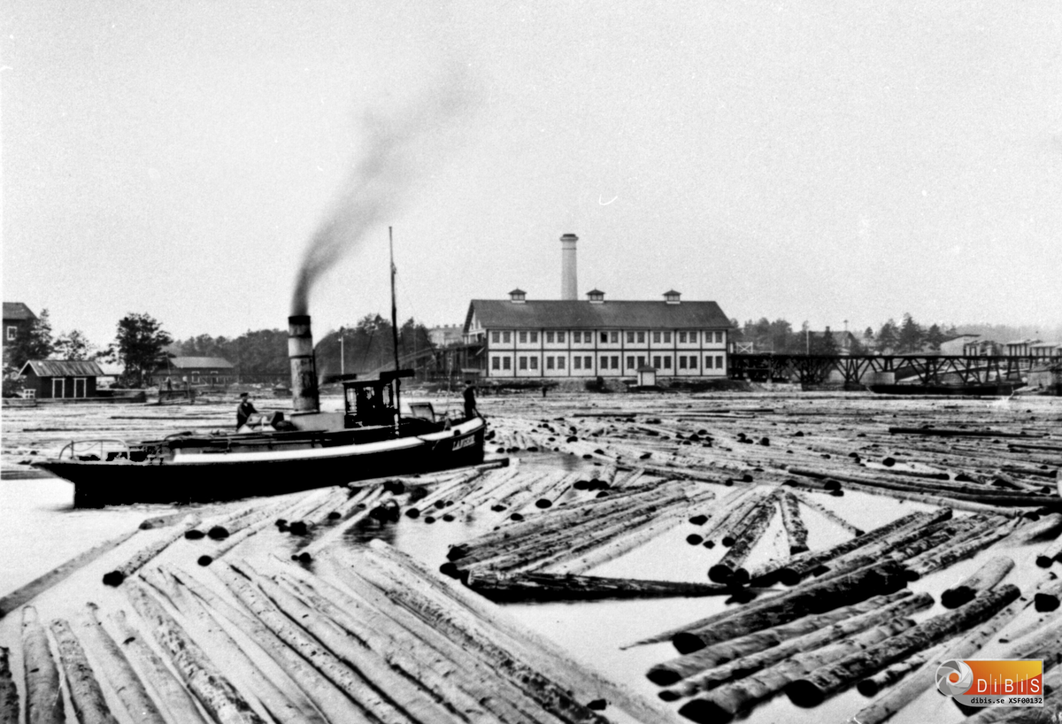 Långrörs sågverk, brädgården till höger. I bakgrunden förvaltarbostaden. Ångbogseraren heter också Långrör (1875-1902). Stångskär skymtar längst till vänster. Detta är den såg som byggdes upp efter 1894 års brand, så fotot troligen från 1895-1902.