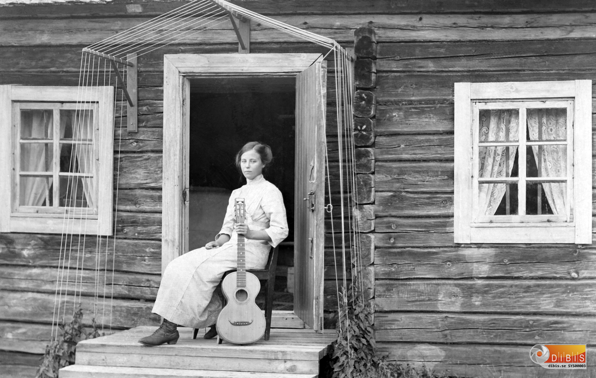 Femsmyra fäbod mellan Villsjön och Bergviken.
Fäbodpigan Stina med sin gitarr, på Femsmyrsstugans bro 1911.