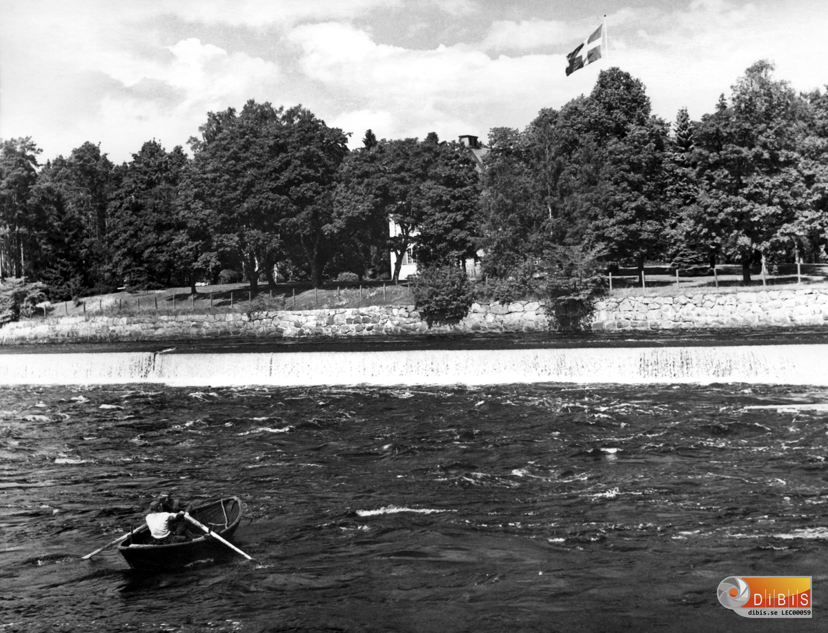 Bakom träden är Ljusnefors Herrgård med sin flagga.
Tjänstebostad åt Disponent Lagerman
I förgrunden laxfiskare som ror ut en laxnot i älven.