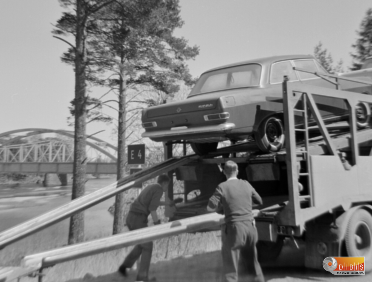 Biltransport på väg norrut på dåvarande E4 på södra sidan av gamla Ljusne bron.
Man fick lasta av de nya personbilarna och köra över dem en och en för att sedan lasta på dem vid Lugnet för fortsatt färd norrut.
Det var vänstertrafik som gällde då.