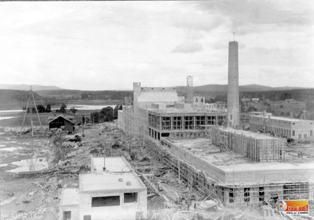 Bild tagen från kabelkrans förartorn 11 aug 1928.
Till vänster i bakgrunden syns kabelkrans rörliga torn, till vänster i förgrunden syns flisrenseriet.
På den långa huskroppen syns närmast pappsalen där man på taket bygger en så kallad lanternin en anordning där fläktar blåser ut överskottsvärme från lokalerna.
Längst bort till höger syns den sedan länge färdiga verkstaden.