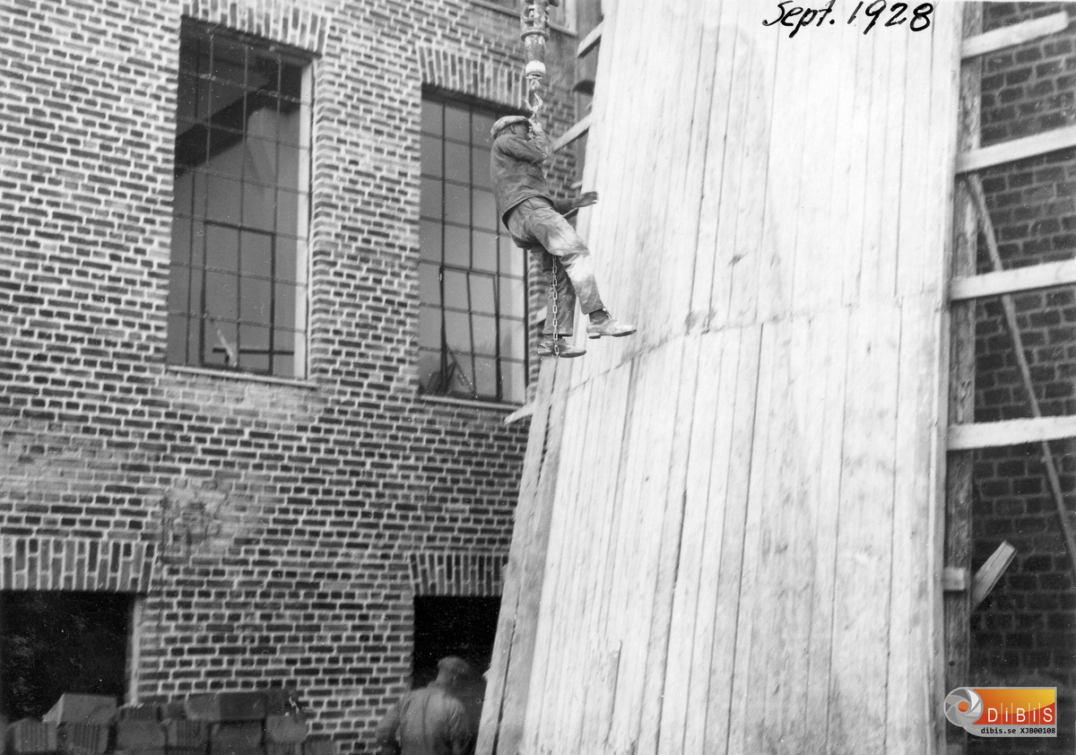 Blid tagen vid foten av skorsten 12 sept.1928.
Murare som är på väg upp till jobbet. Med ena foten i en kättingögla sen gäller det att hålla i sig.