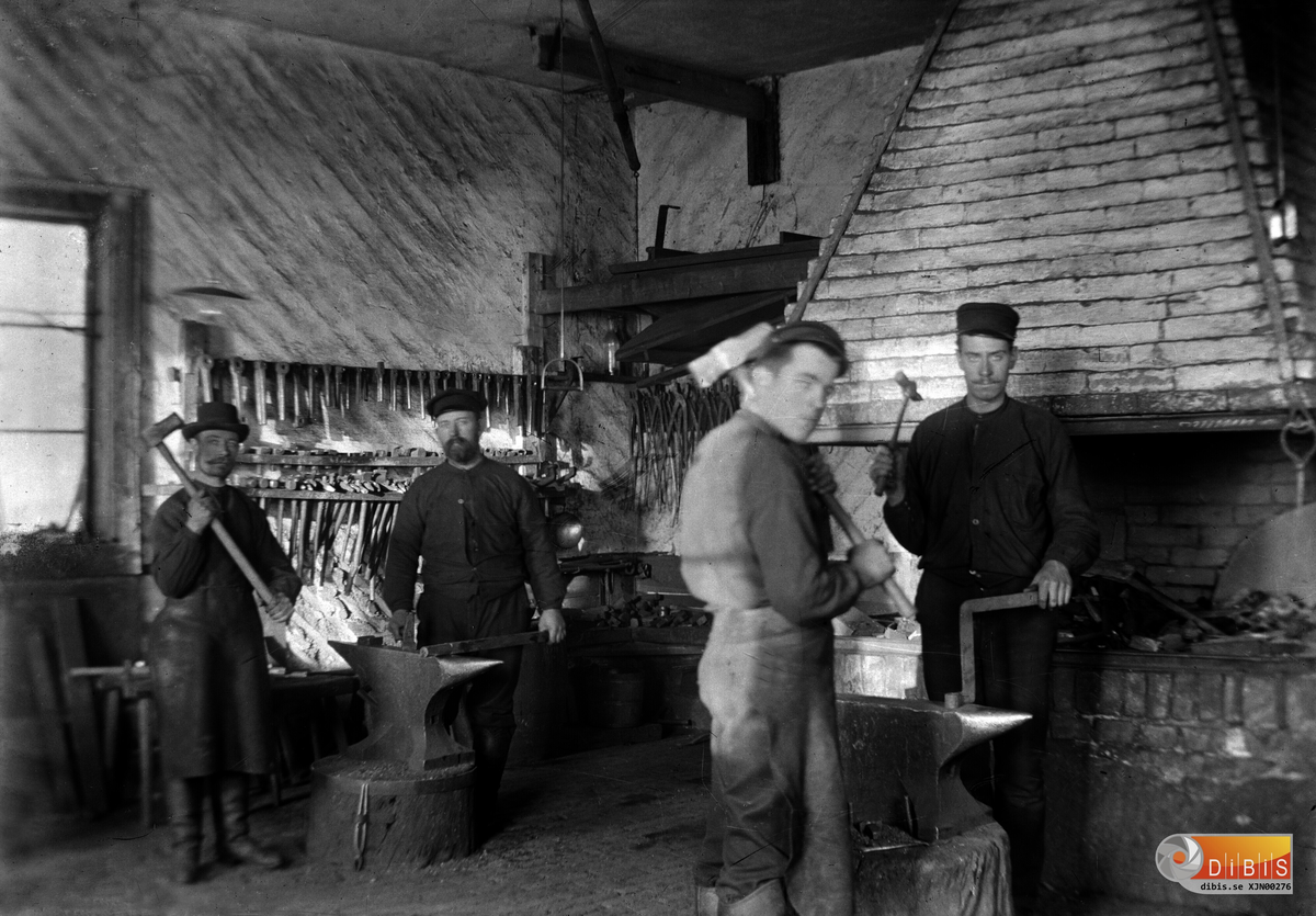 Interiör från smedjan vid sågen. Smederna är Alfred Nykvist och Vilmer Spansk, slägg-drängen till höger är Ludvig Nyblad.