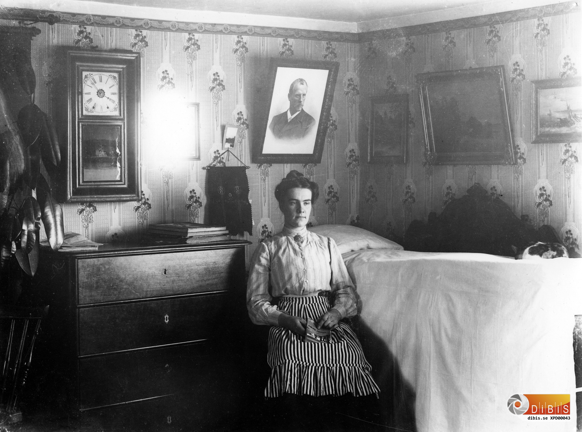 Interiörbild från fotografens hem.
Dottern Jenny Lind sitter vid den uppbäddade sängen.
