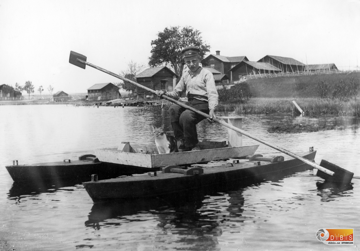 Herman Lind i kanoten på Föltjärn med katten i sällskap.
I bakgrunden ser man Fältens gård, Ramens lider och härbre längre bort, samt längst till vänster gaveln på Jonanders ladugård. Omkring 1906-08.