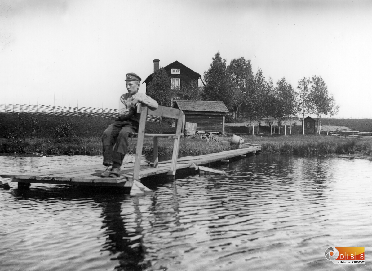 Per Lind ute på bryggan vid Föltjärn, med hemmet i bakgrunden. Omkring 1906-07.