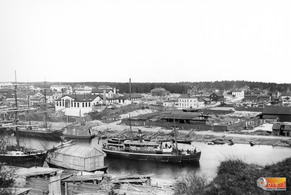 Vy från Faxeholmen mot norra delen av staden. Söderhamns Mekaniska Verkstad mitt i bilden. Bland segelskutor och virkespråmar är ett ångfartyg på utgående mot fjärden.