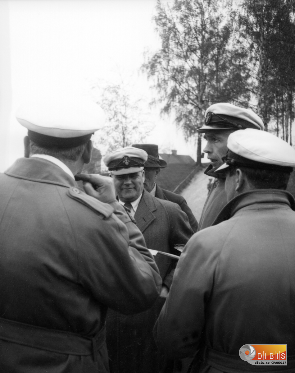Fem Man, fyra av dom har mössor med märken, med bokstäverna HMK - Hälsinglands Motorklubb bildad i Bollnäs 1921. Automobil historiska klubben startades omkring 1960. I mitten Petrus Sköld, Bollnäs, Hälsinglands MKs första ordförande 1921-1931.