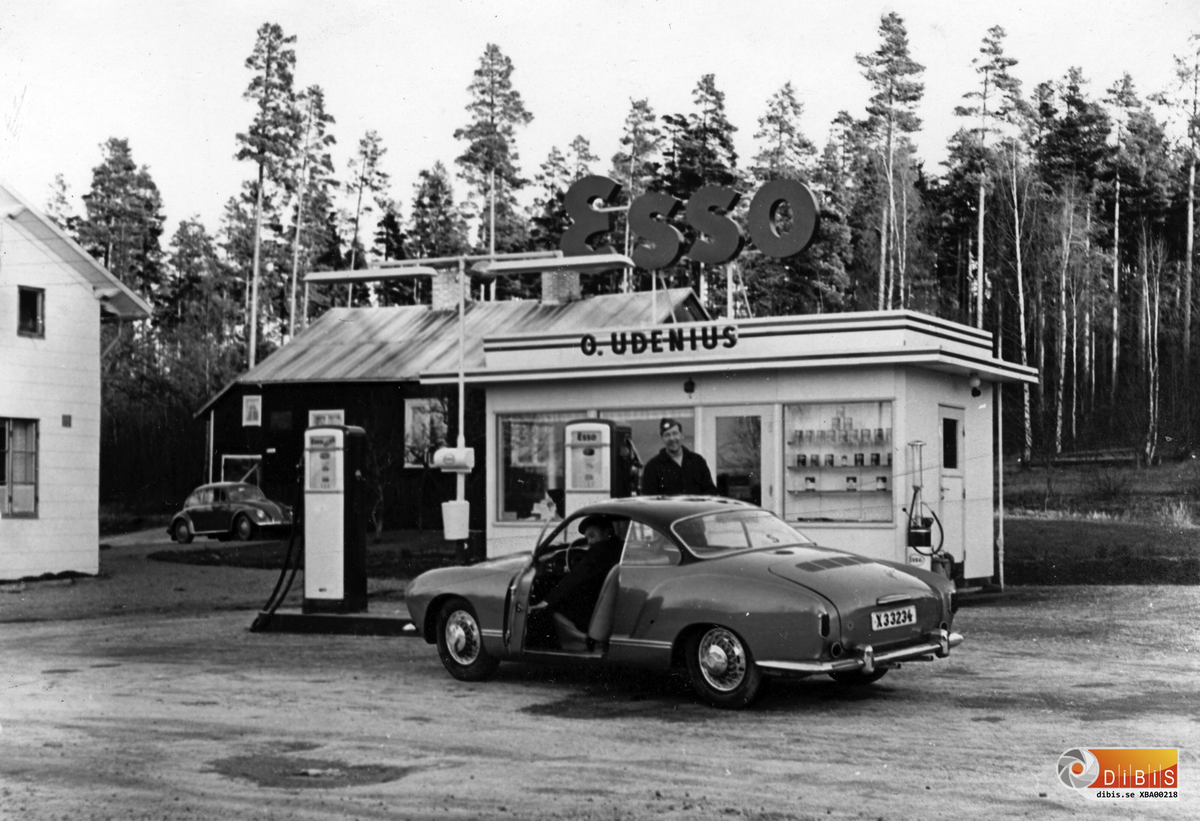 Olle Udenius vid den mack han tagit över efter sin svärfar. Hans yrke var dock bagare och han gjorde ingen hemlighet av att han föredrog mjöl framför motorolja.
I bilen Roland Stenberg som senare flyttade till Lillhärdal.
Roland var elektriker på Vansäterfabriken i mitten av 1960 talet. Han var också en inbiten sportflygare och flög många pass för brandflyget i Mohed.
Bilen en Carman Ghia på VW-shassi
Till höger om kiosken syns en bensinpump för mopeder. I bakgrunden den byggnad som innehöll ett bageri. Byggnaden eldhärjades senare.
