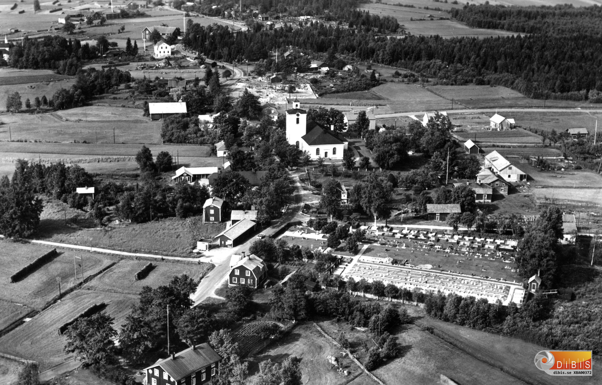 Ett flygfoto över Skog med kyrkan, den närliggande kyrkogården, Gottfrid Bergströms kiosk och lantbruket i socknens centrum.