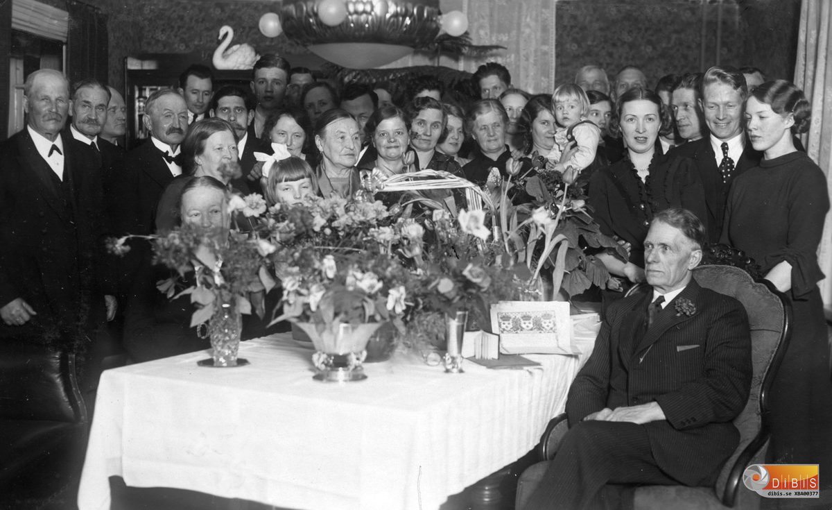 Magnus Elmblads sittande i fåtöljen, firar sin 70-årsdag i sitt hem i Bergvik. Han blev änkeman 1933. Den vita svanen till vänster om takkronan fick han när han fyllde 50 år.

Bakom Magnus, till höger, står yngsta dottern Emy, född 1915.
Till vänster om henne står dottern Sigrid, född 1910.
Mellan dem står sonen Tage  född 1912. Bakom Tage finns sonen Erik född 1900. Hans hustru Regina står till vänster med deras enda barn, Lennart, i famnen. (Erik m familj bodde kvar i Bergvik till Eriks död 1963.)

Framför svanen står Petrus Zettersten som framför sig till höger har N.O. Björklund, Bäckfors, och till vänster Emanuel Zettersten.
Framför dessa tre står Elin Björklund och till höger om henne Lisa Engvall som var gift med pastor Gustav Engvall som står skymd i sällskapet..
Nr 2 från vänster är Oskar Bergstrand, Regina Elmblads far.