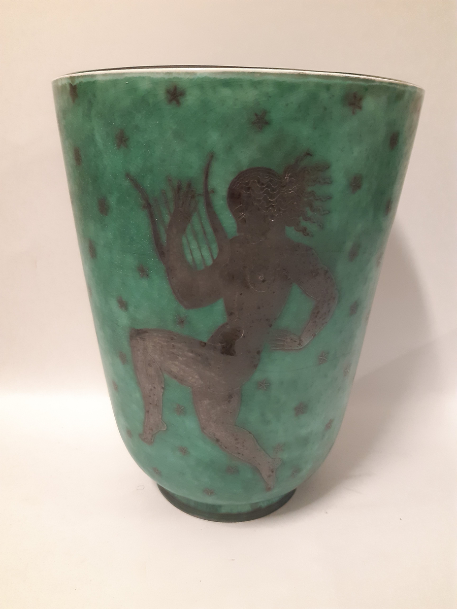 Stor vas i argenta med silverdekorationer föreställande tre dansande musikanter mot grön glasyr, en spelar dubbelfjölt, en spelar lyra och den sista spelar cymbaler.
