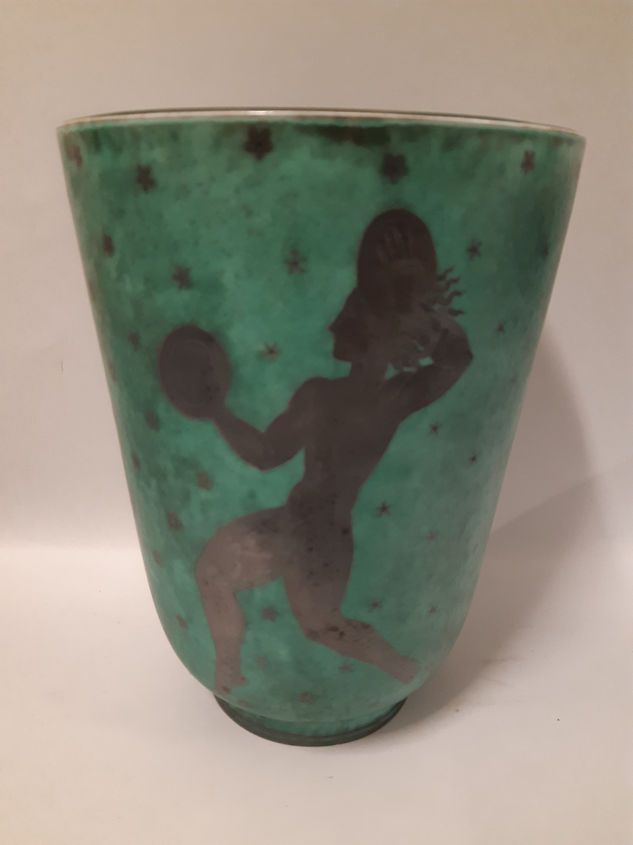 Stor vas i argenta med silverdekorationer föreställande tre dansande musikanter mot grön glasyr, en spelar dubbelfjölt, en spelar lyra och den sista spelar cymbaler.
