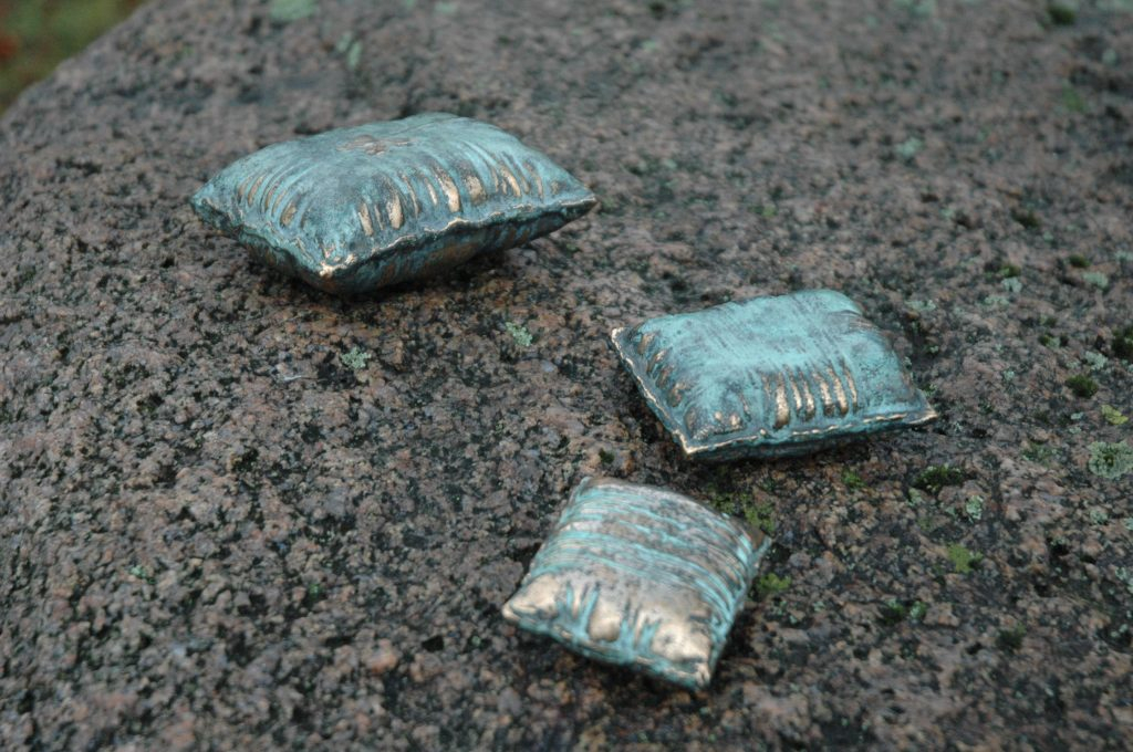 REM består av tre miniatyrskulpturer i brons, formade som kuddar – symboler för övergångar mellan verklighet och dröm. Varje kudde bär på en berättelse om bronsens eviga kretslopp: från konst och kyrkklockor till krigets kanoner, och tillbaka till konsten.

Här vilar drömmar, fångade i bronsens tyngd och tidlöshet, en påminnelse om att det dolda och oupptäckta alltid väntar på att upptäckas.heten att vara den/det man är.

Skulpturen monteras på en aluminiumplatta som fästs med två skruvar. Underlaget behöver en fördjupning, sedan limmas med epoxylim – förslagsvis på sten eller betong.