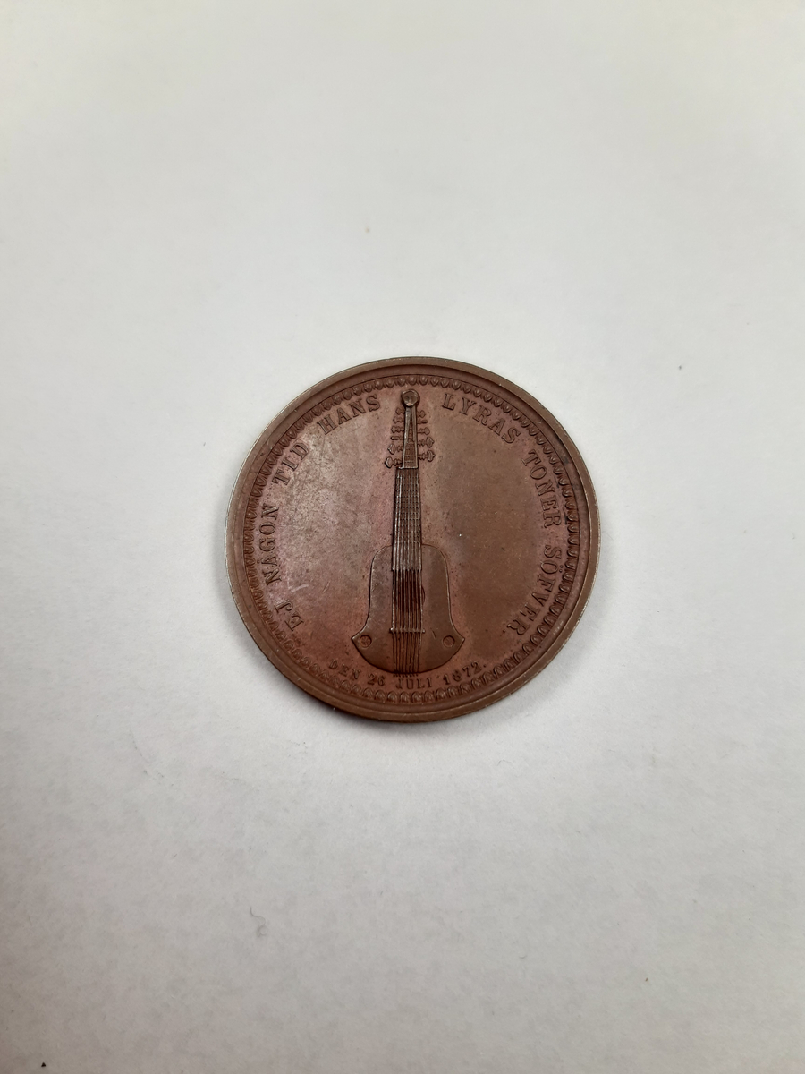 En bronsmedalj, på åtsidan finns ett mansporträtt i profil, frånsidan finns det relief föreställande en halscittra.
