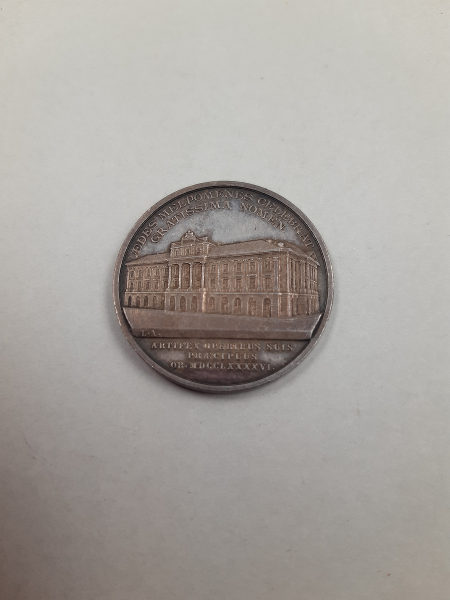 Silvermedalj med reliefdekor, på åtsidan ett mansporträtt i profil och på frånsidan Operahuset i Stockholm.
