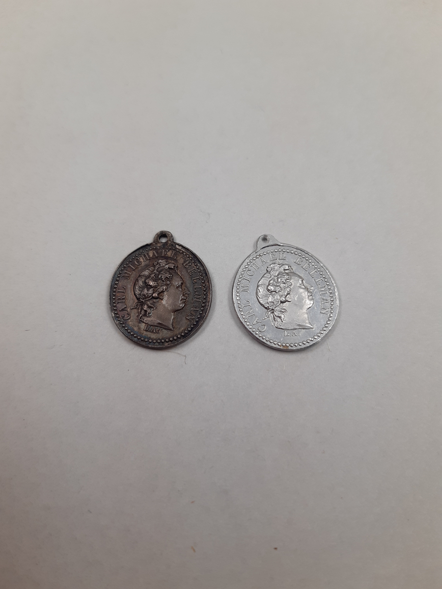 Två ovala silvermedaljer, på åtsidan finns ett mansporträtt i profil, frånsidan finns det relief föreställande en halscittra.
