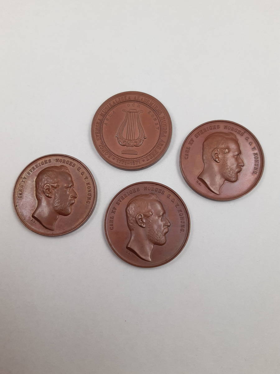 Bronsmedalj kung Carl XV porträtt i profil på åtsidan och en lyra på frånsidan.
