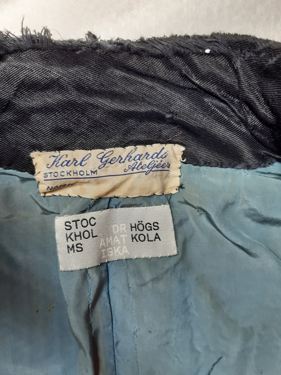 Uniformsjacka av ull i ljusblå färg. Jackan är en kort modell, sk. dolma eller attila. Rikt dekorerad med snoddar, snörmakeri och fransar i guldfärg med en textil kärna. Flätade snoddar på axlarna och en ägiljett runt vänster axel. Klotformade knappar av metall mitt fram, på framstycket och på axlarna. Ståkrage med hyska och hake mitt fram. Fodrad med ett ljusblått tyg med bröstfickor på varje sida. Hakar längs nederkantens insida.
