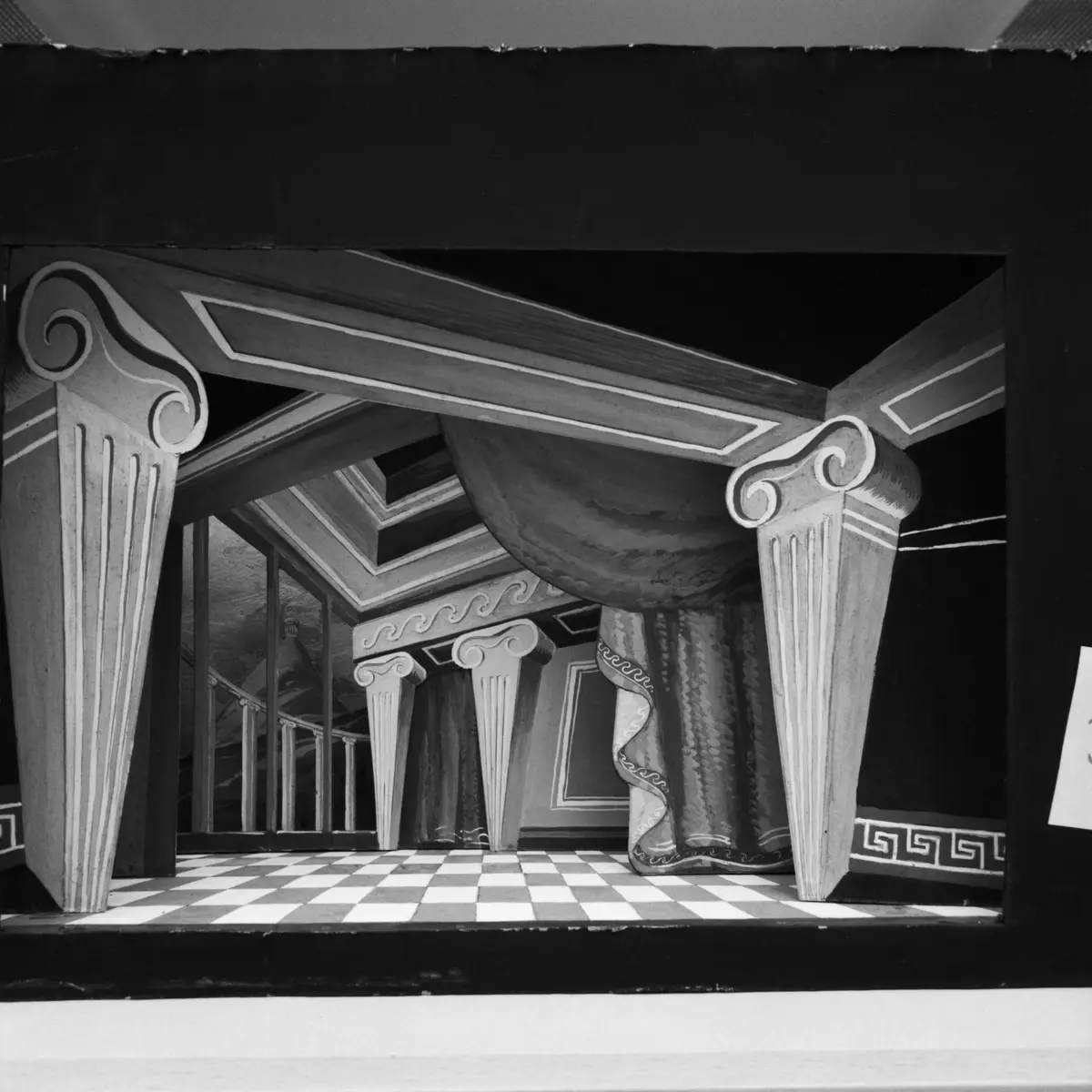 Ett gemak med stiliserade joniska kolonner som uppbär bjälklag, röda draperier med blå bård. Perspektiven oregelbundna. Till vänster genom ett gallerverk en utsikt mot ett berglandskap med ett litet tempel. Golvet är schackrutemönstrat i grått och vitt. 
