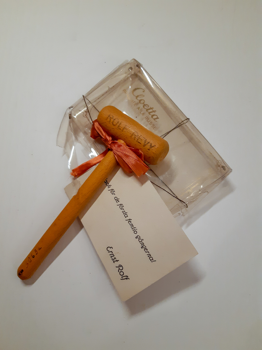 A - Liten röd träklubba med tryck, en torkad liten blomsterbukett och ett visitkort fästade med papperssnöre på ett vishäfte. På vishäftet finns ett stilerat porträtt av Ernst Rolf med konstnärssignatur "E-N" Einar Nerman.
B - Lite ofärgad träklubba med text och ett visitkort fästade med rött sidenband på ett plastetui/hölje för choklad.
C - 3D-glasögon i vit papp med ett rött och ett blått öga i plast. Reklamtext för Buick.
