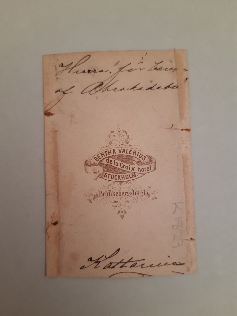 Sepiafärgat fotografi föreställande en kvinna klädd som en renässansyngling i höga stövlar, knäbyxor, väst, jacka och kort mantel. I handen håller hon en fjäderbrydd hatt.
