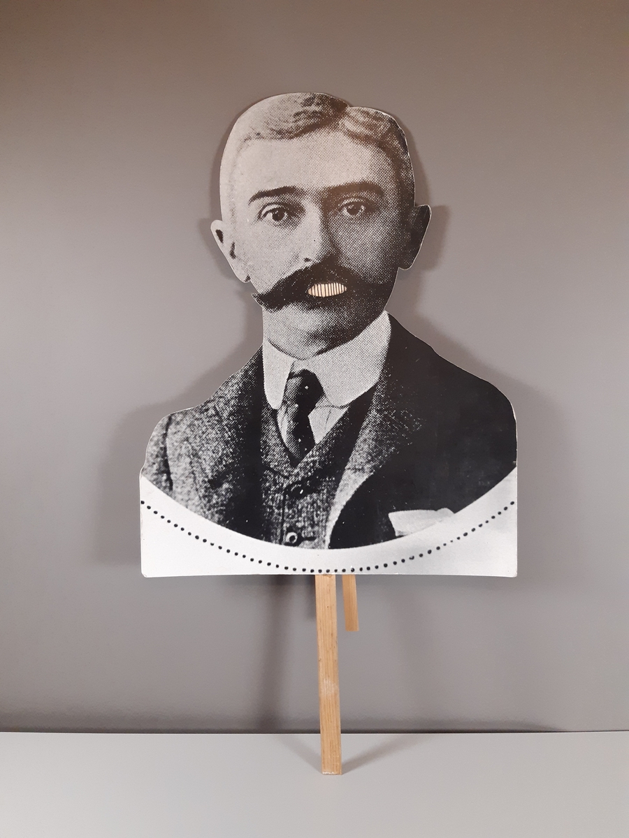"Pratande" man tillverkad av ett uppförstorat svartvitt fotografi. Huvud, hals och axlar är utklippt. Mannens mun går att öppna och stänga med en träkonstruktion med två handtag på baksidan.
