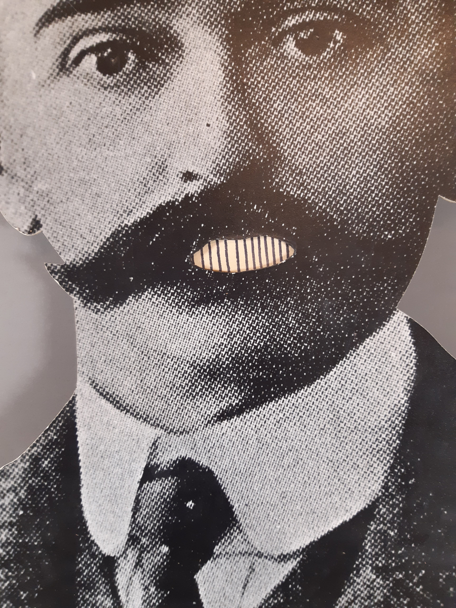 "Pratande" man tillverkad av ett uppförstorat svartvitt fotografi. Huvud, hals och axlar är utklippt. Mannens mun går att öppna och stänga med en träkonstruktion med två handtag på baksidan.
