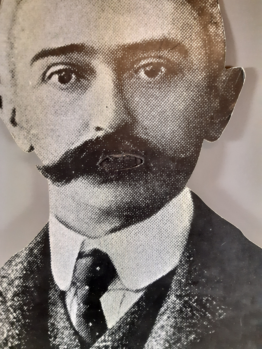 "Pratande" man tillverkad av ett uppförstorat svartvitt fotografi. Huvud, hals och axlar är utklippt. Mannens mun går att öppna och stänga med en träkonstruktion med två handtag på baksidan.
