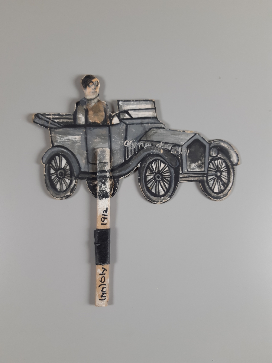 Dubbelsidig T-Ford med förare målad på kartong på skaft.
