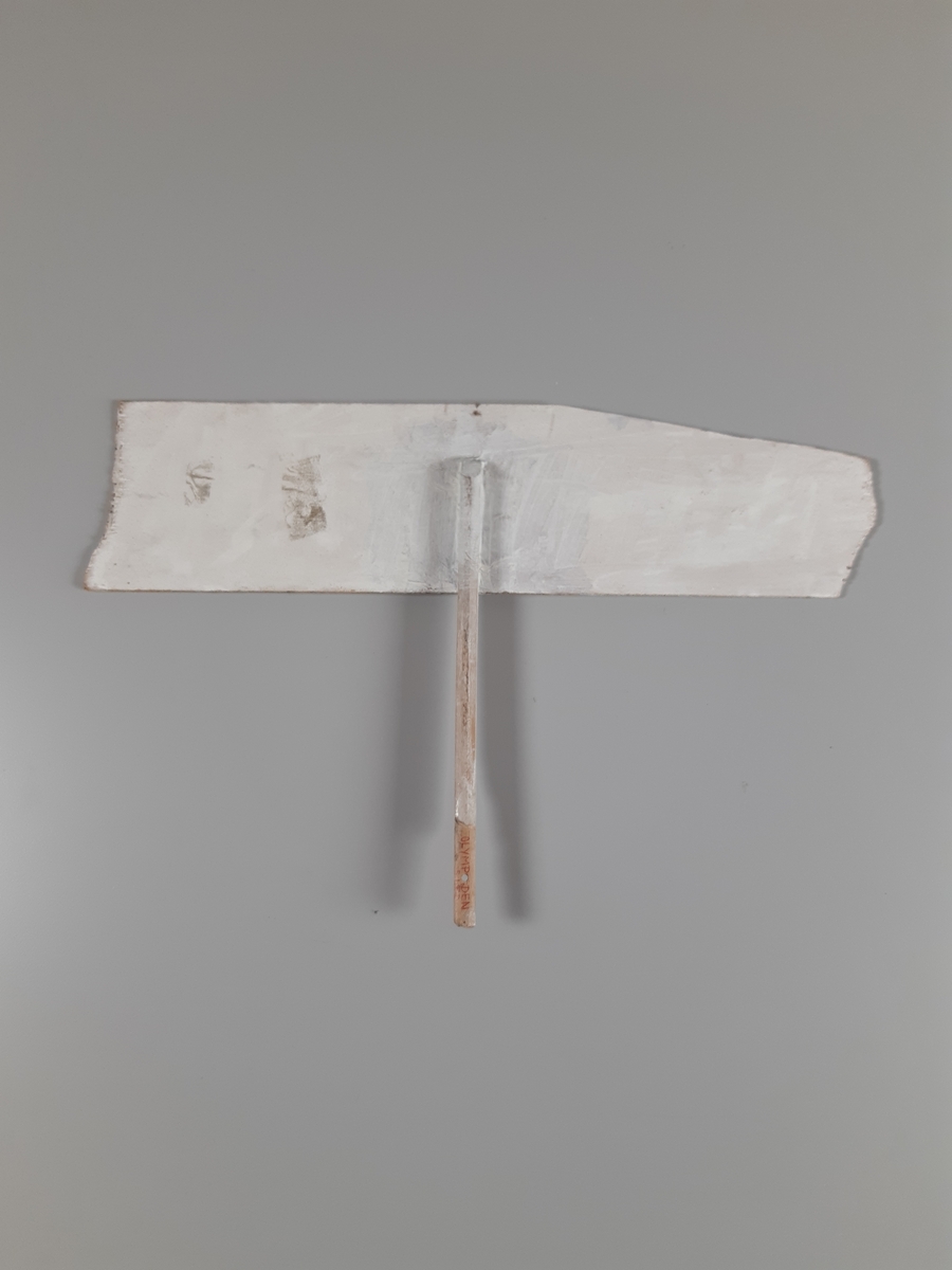 Vitmålad skylt med svarta bokstäver med skaft.
