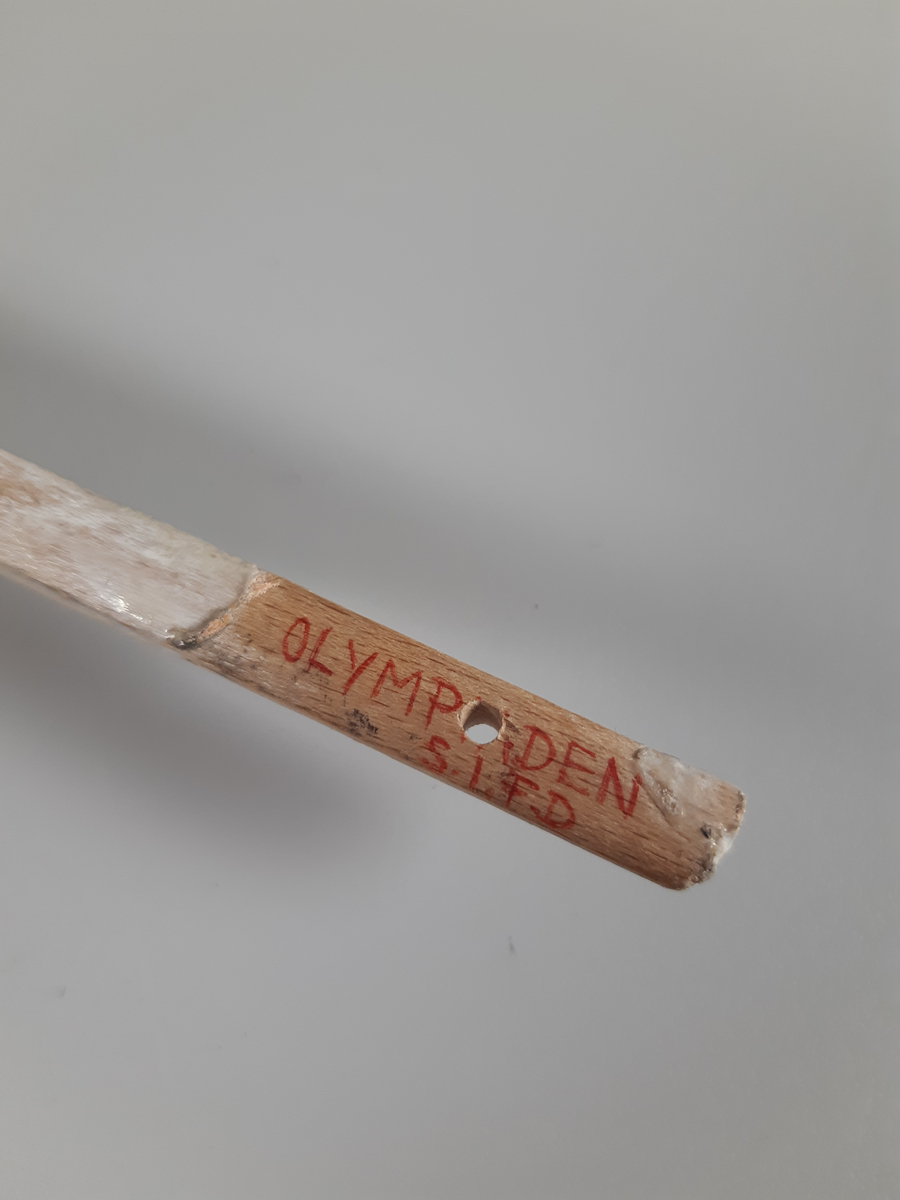 Vitmålad skylt med svarta bokstäver med skaft.
