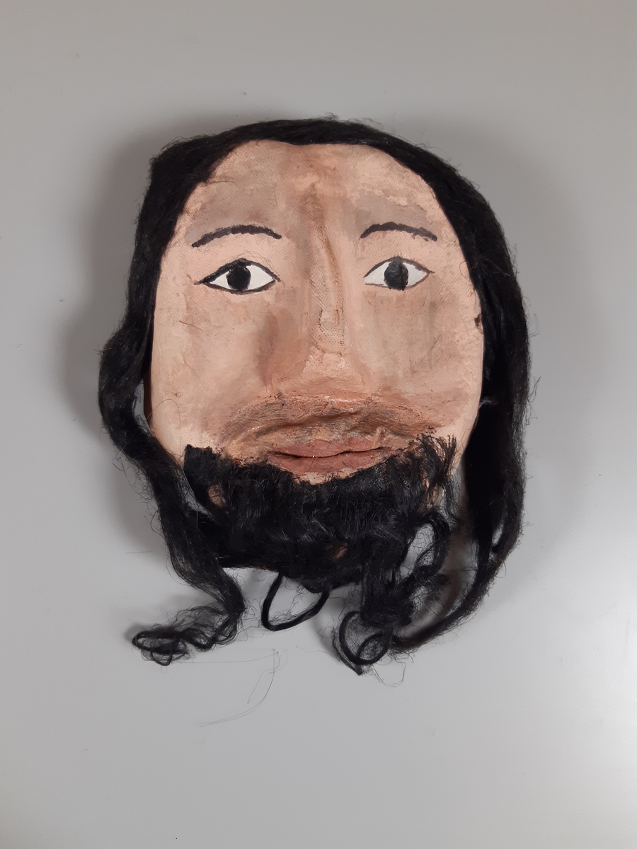 Mask föreställande man med mörkt hår och skägg.
