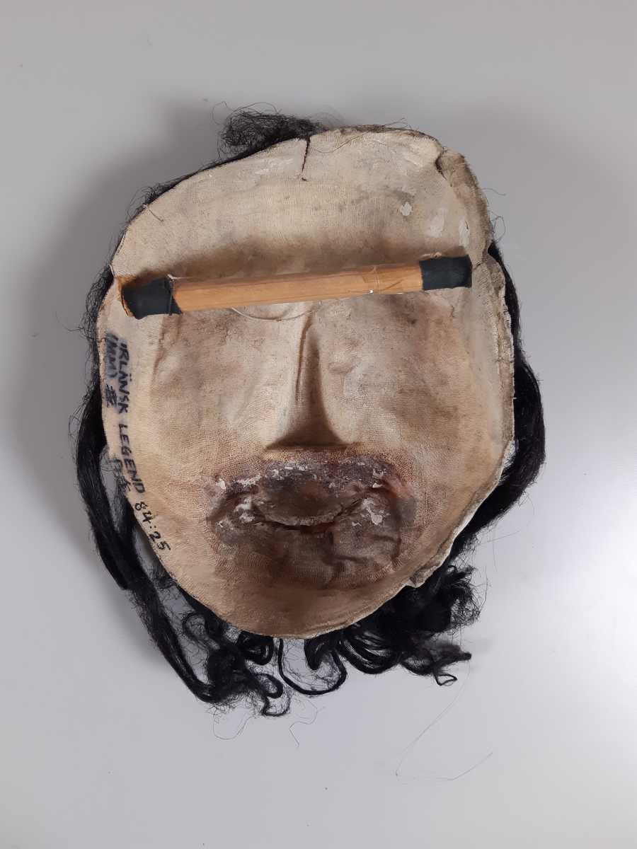 Mask föreställande man med mörkt hår och skägg.
