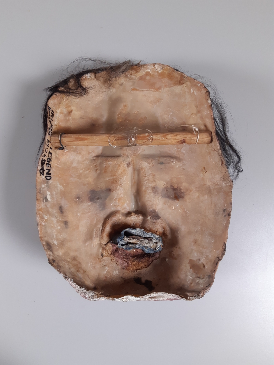 Mask föreställande man med kort mörkt hår.
