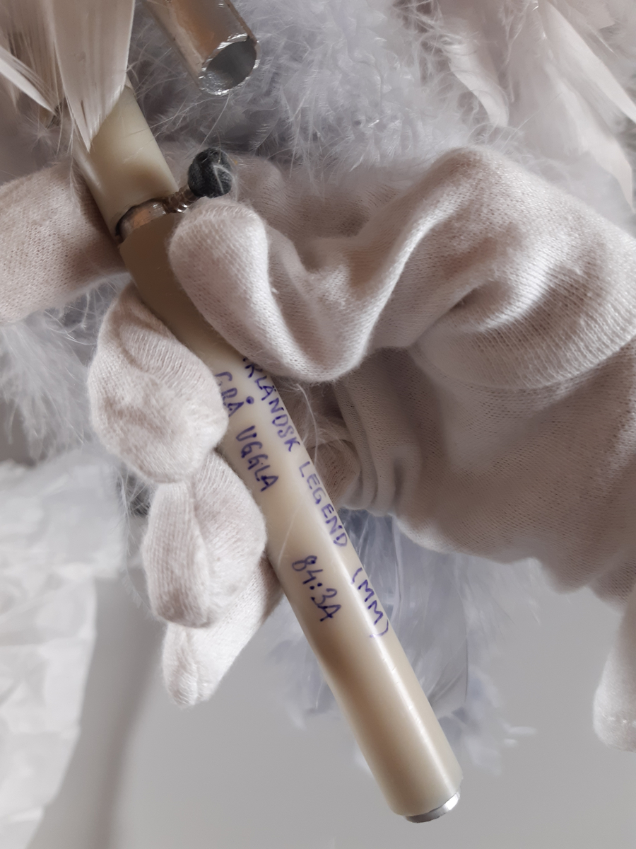 Uggla med huvud och vingar av gips, klädda i ljusgrå fjädrar, kroppen tillverkad av en fjäderboa. Fötter och nädd är i gummiliknande material. Ugglan har ett plaströr i ryggen som handtag samt en liten spak för att kunna röra ögonen från sida till sida.
