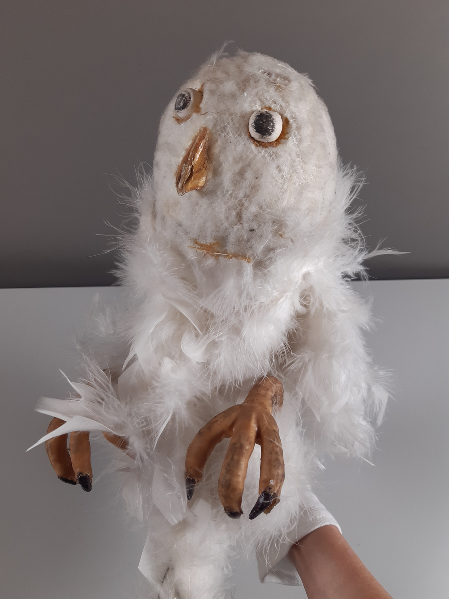 Uggla med huvud och vingar av gips, klädda i vita fjädrar, kroppen tillverkad av en fjäderboa. Fötter och nädd är i gummiliknande material. Ugglan har ett plaströr i ryggen som handtag samt en liten spak för att kunna röra ögonen från sida till sida.
