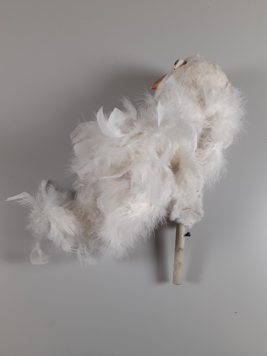 Uggla med huvud och vingar av gips, klädda i vita fjädrar, kroppen tillverkad av en fjäderboa. Fötter och nädd är i gummiliknande material. Ugglan har ett plaströr i ryggen som handtag samt en liten spak för att kunna röra ögonen från sida till sida.
